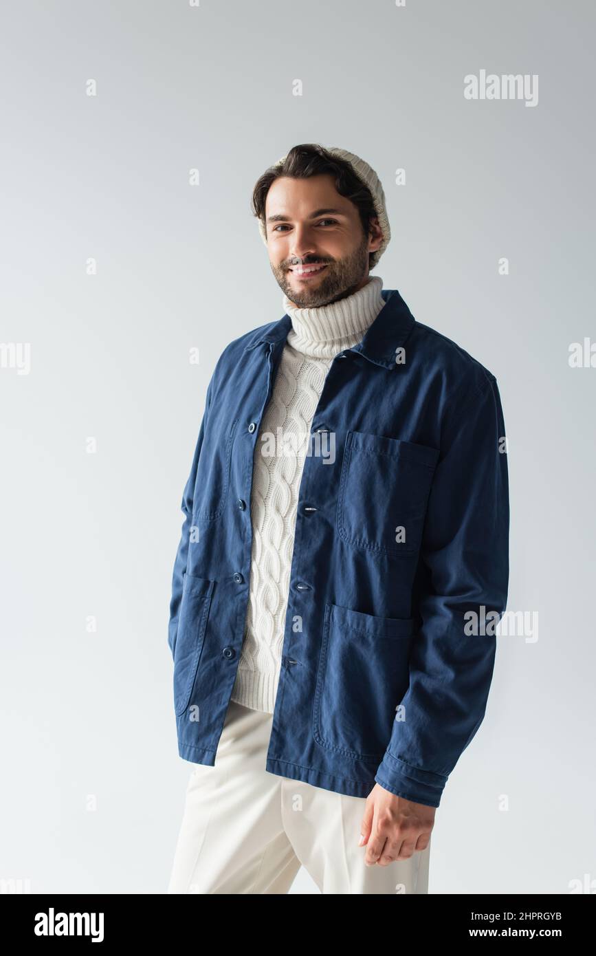happy man in blue jacket and white knitted sweater smiling at camera isolated on grey Stock Photo