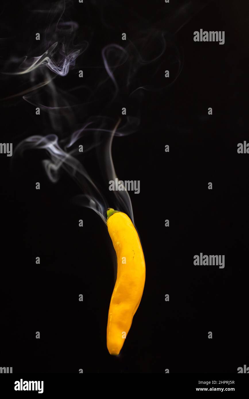 Yellow hot Mexican chili peppers against a black background with smoke