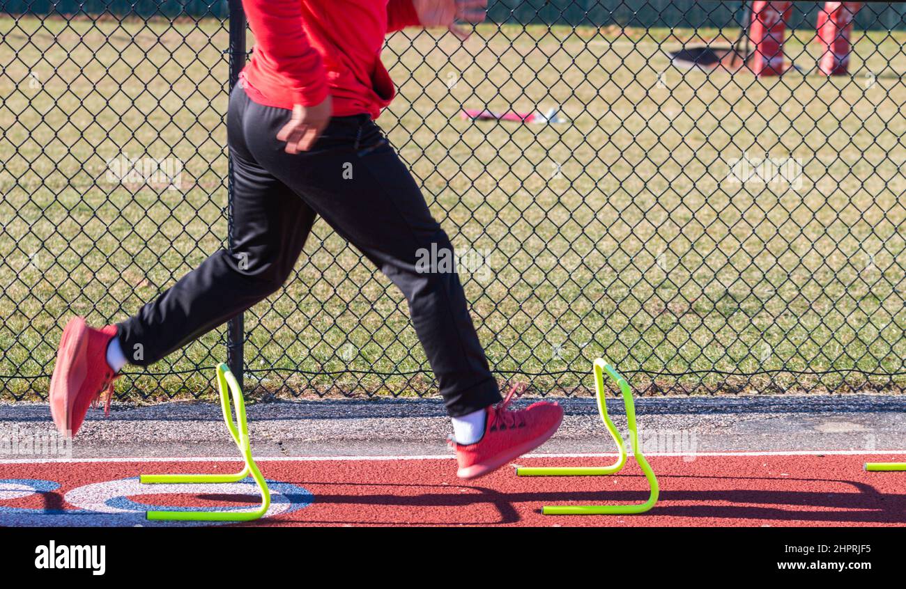 A high school track runner reunning over small hurdles on a track
