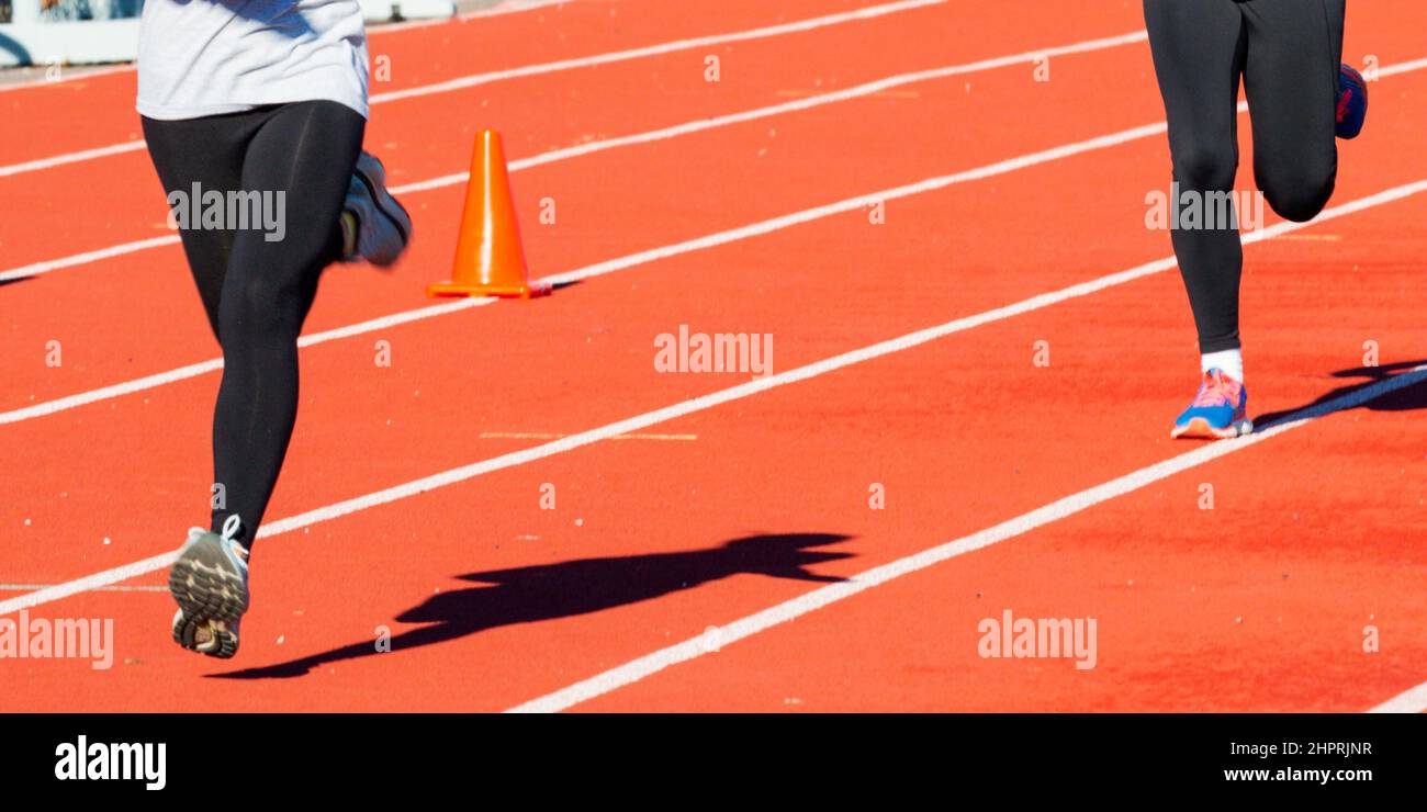 Two girls wearing black spandex while running fast on a red track past