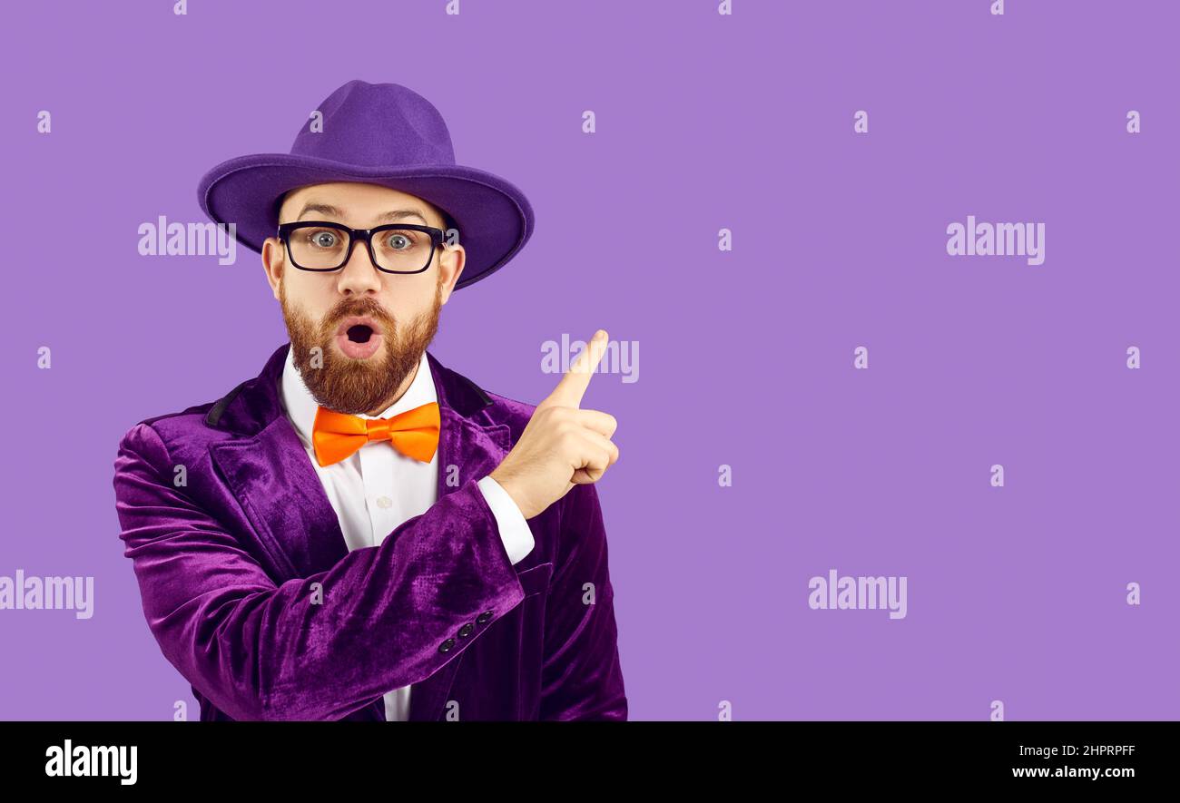 Man with surprised expression on his face points his index finger at copy space on purple background Stock Photo