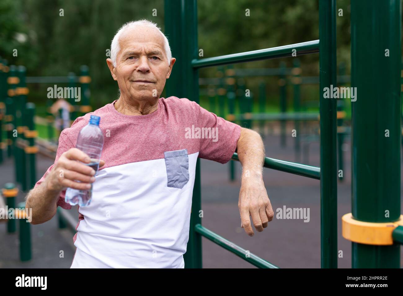 Senior man resting and drinking water from bottle after jogging in park ...