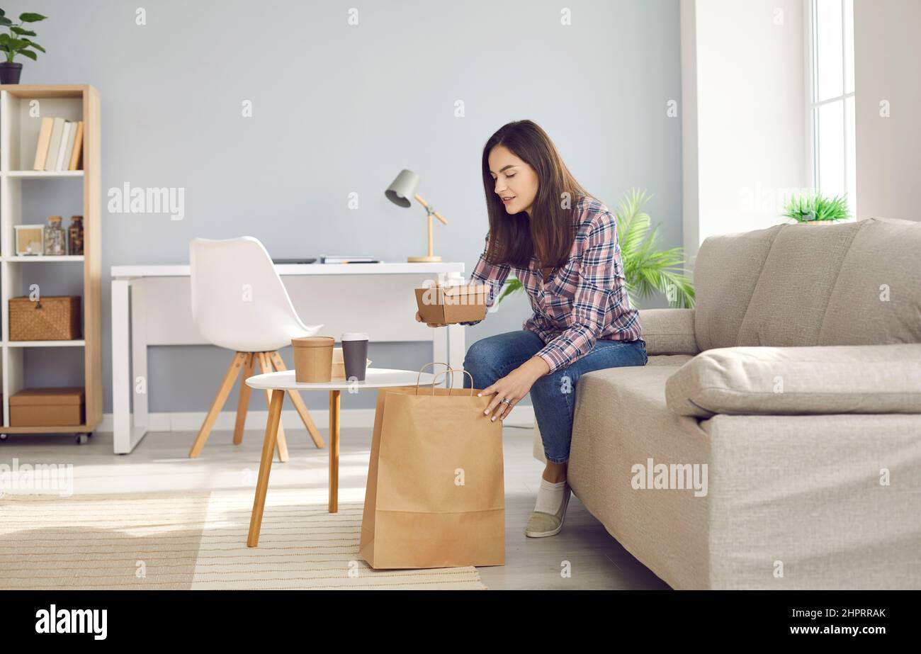 Young woman sitting on couch and unpacking her takeaway lunch from meal delivery Stock Photo