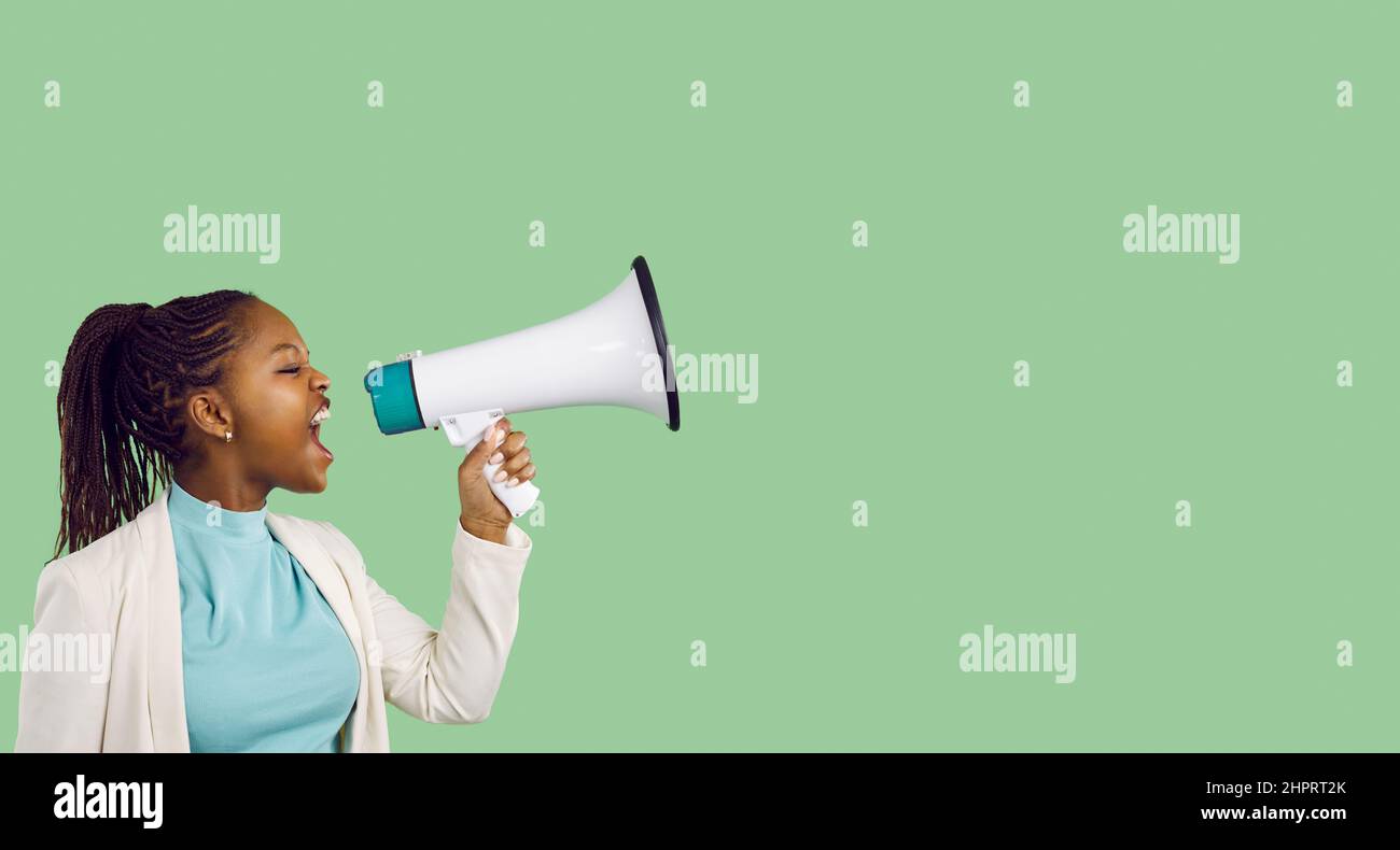 Young black woman shouting through megaphone on green copy space banner background Stock Photo