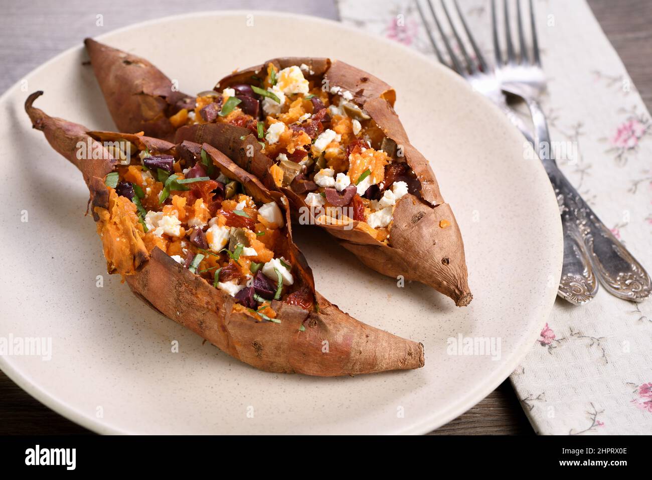 Baked sweet potato stuffed with chopped sun-dried tomatoes, olives, feta cheese and basil with aromatic dressing Stock Photo