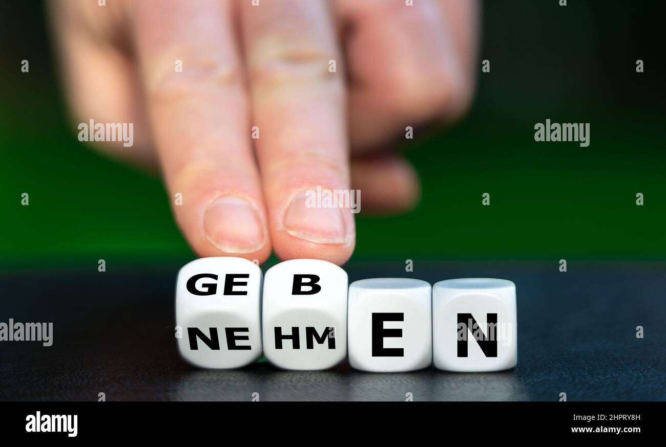 Hand turns dice and changes the German word 'nehmen' (take) to 'geben' (give). Stock Photo
