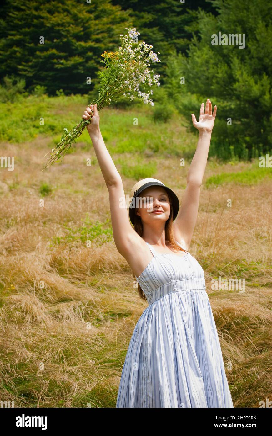 Young woman standing in a field holding up a bouquet of wild flowers ...