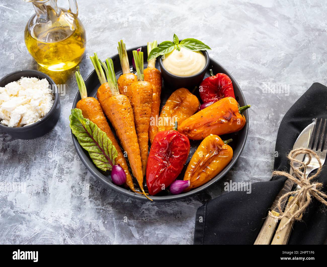 baked roast baby carrots, bell pepper in a plate, basil and spices vegan dish close up, white sauce, close up Stock Photo