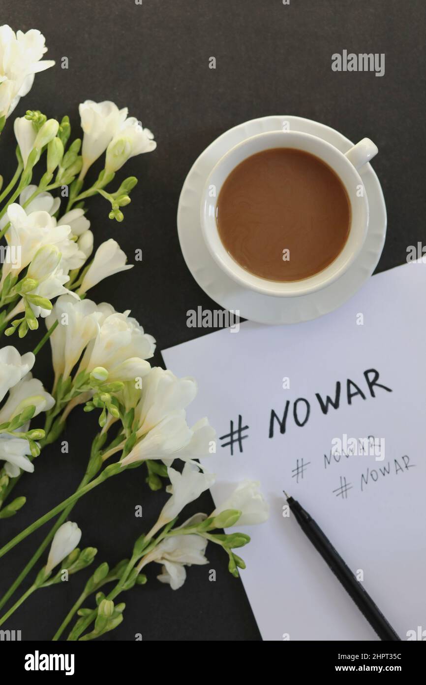 No War message on white paper, cup of coffee and white flowers on dark background. Copy space Stock Photo