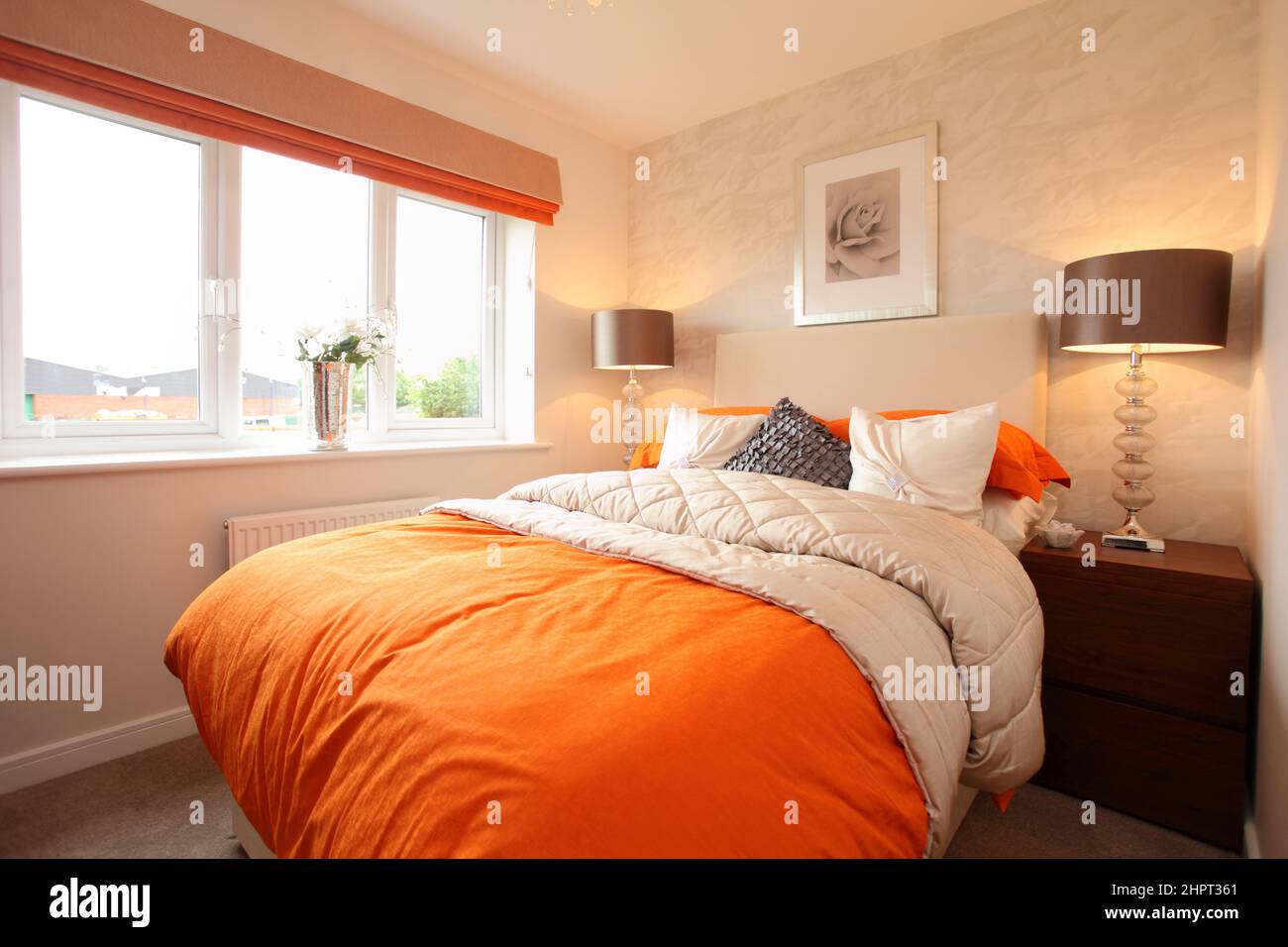 Vivid orange decor bedspread and cushions in a modern bedroom scene setting. Stock Photo
