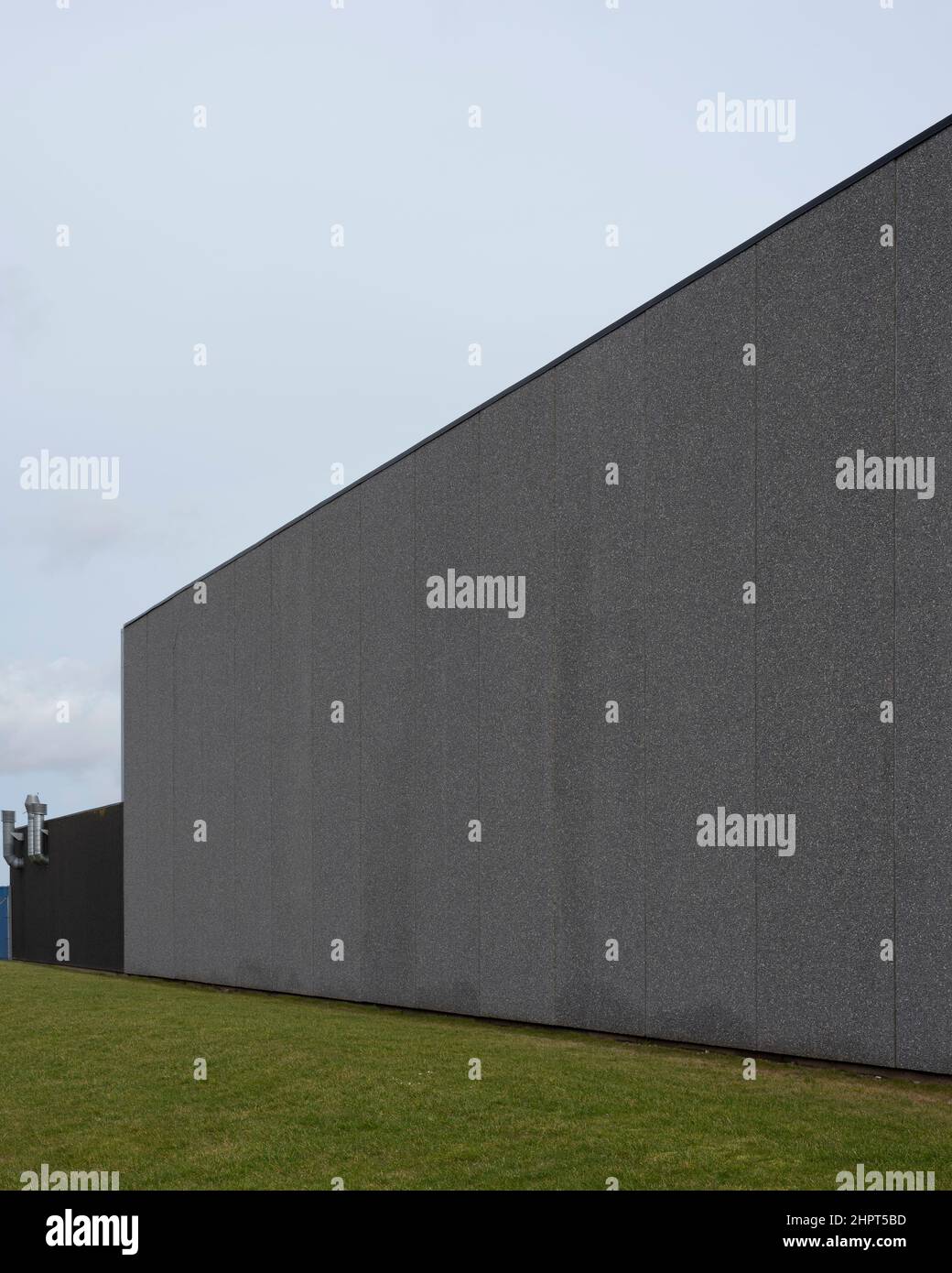 an empty gray wall on a warehouse building in gray concrete and a lawn in the foreground, Frederikssund, Denmark, February 22, 2022 Stock Photo
