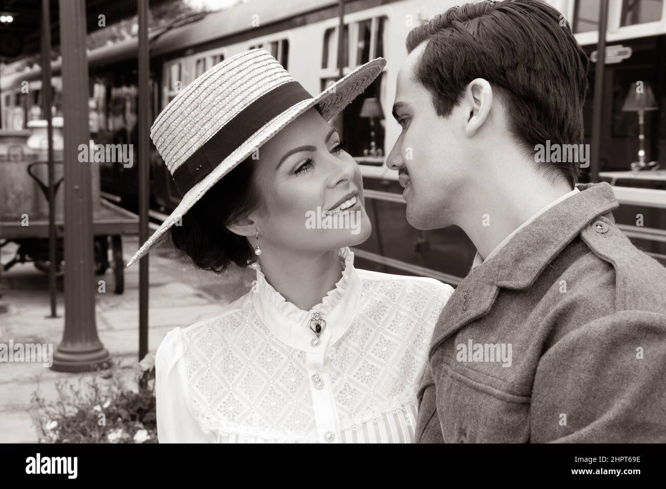 Vintage couple, man in uniform, woman in dress and hat, about to kiss at railway station with train in background Stock Photo