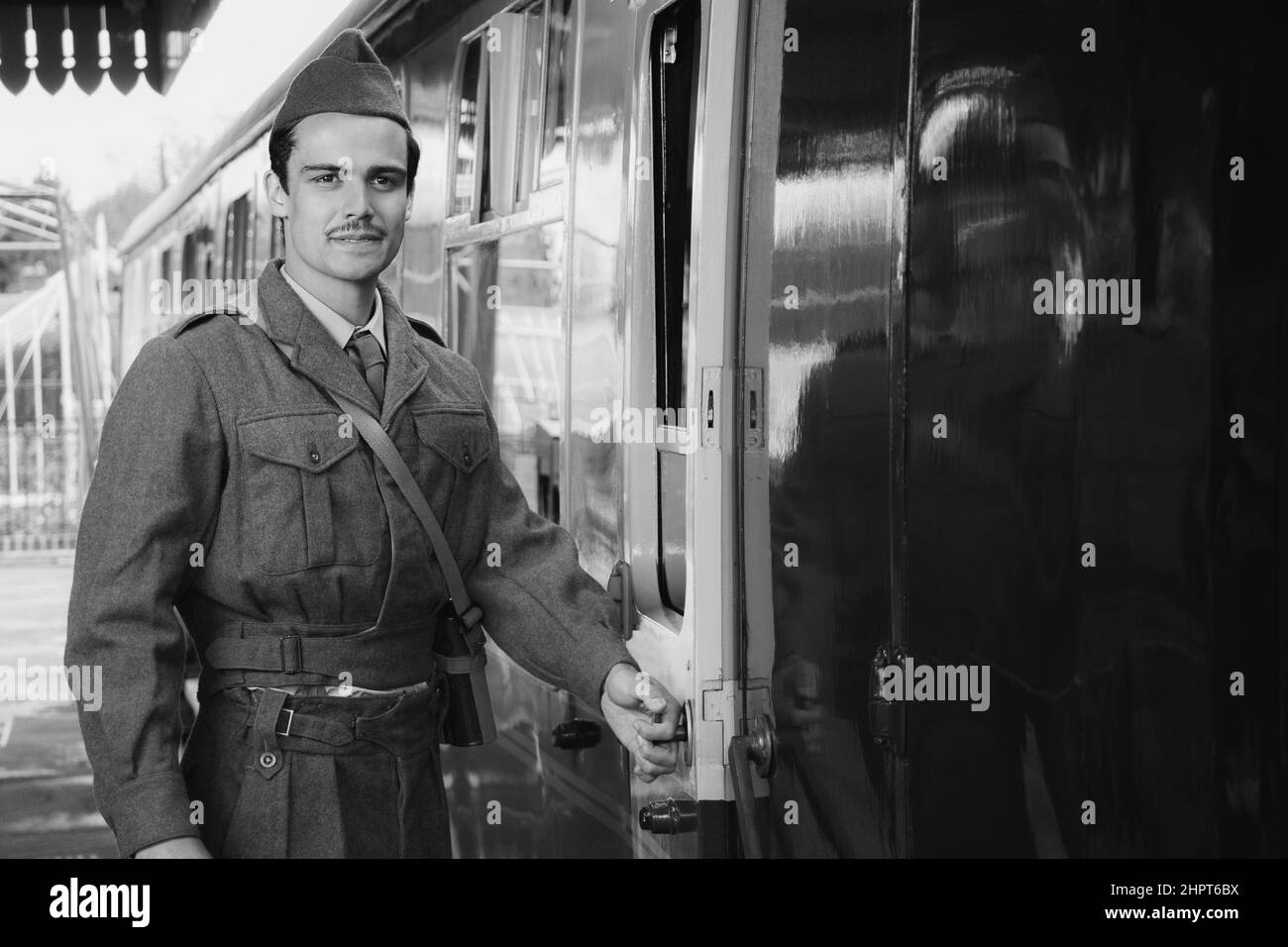 Attractive male british soldier in vintage WW2 uniform at train station standing next to train looking pensive Stock Photo