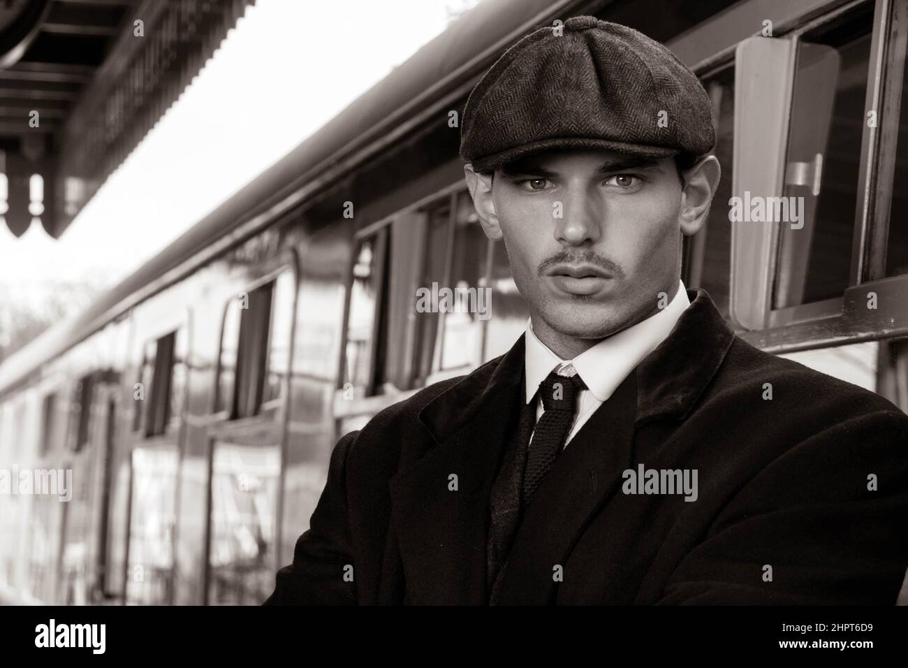 Attractive English gangster with cigarette leaving train at railway station Stock Photo