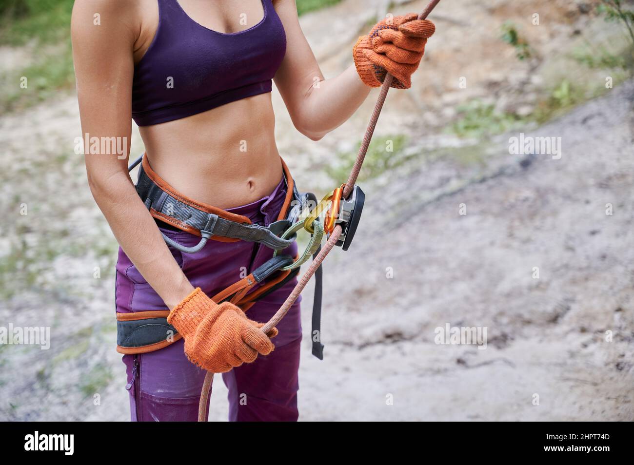 Close up of young female climber belaying leader during rock climbing outdoors, using rope, grigri, carabines and gloves. Concept of teamwork, trust, extreme sport and outdoor activity. Stock Photo