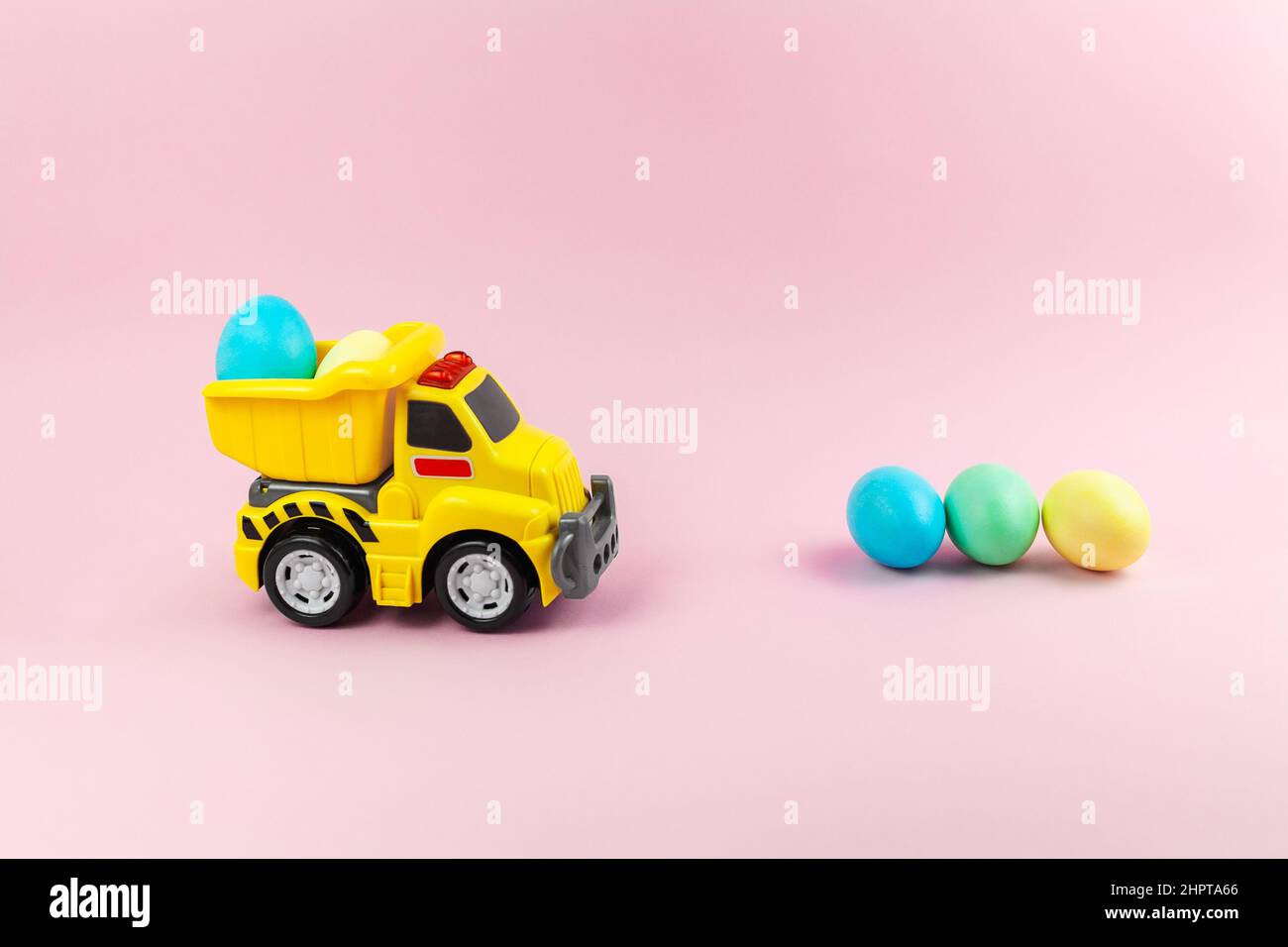 A toy yellow truck carrying Easter eggs in pastel colors. Easter card with place for text on a pink background. Easter food delivery Stock Photo