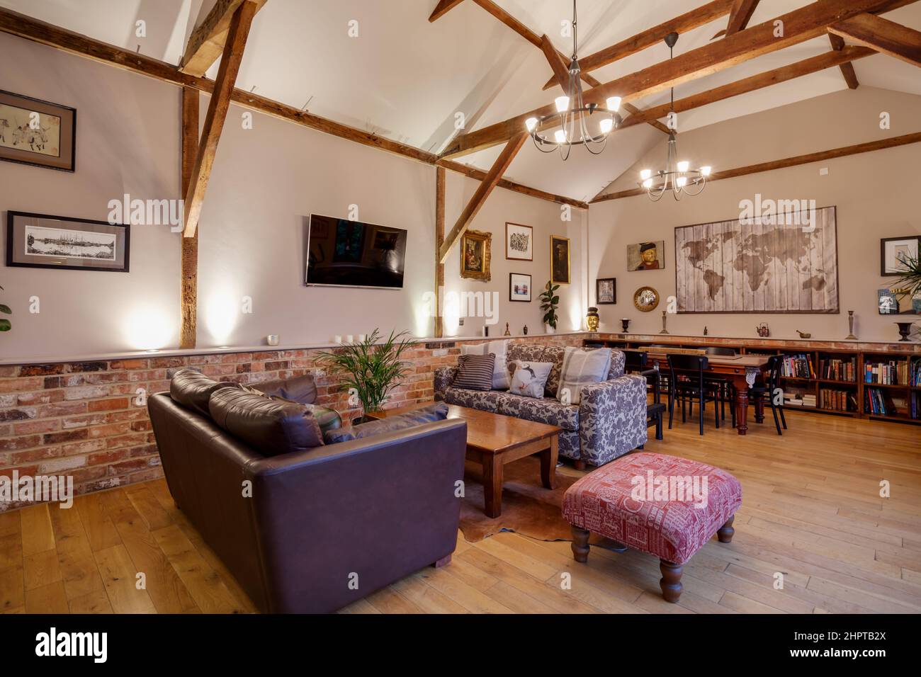 Traditional lookingh furnished vaulted living room within converted barn building with open plan to dining area with sofas, coffee and dining table. Stock Photo