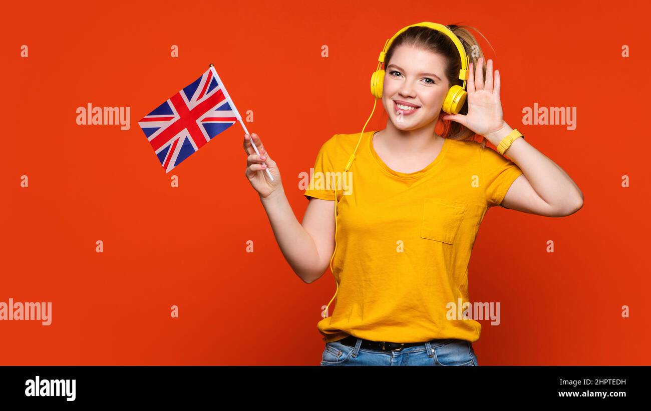 Girl in yellow basic suit and headphones holds small UK flag. Study