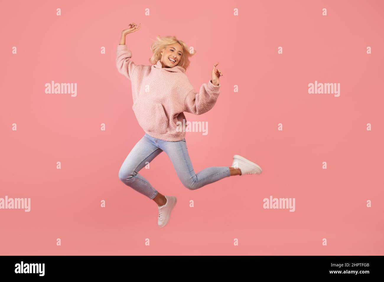 Successful moment. Excited young lady jumping and having fun, being in good mood, celebrating triumph, pink background Stock Photo