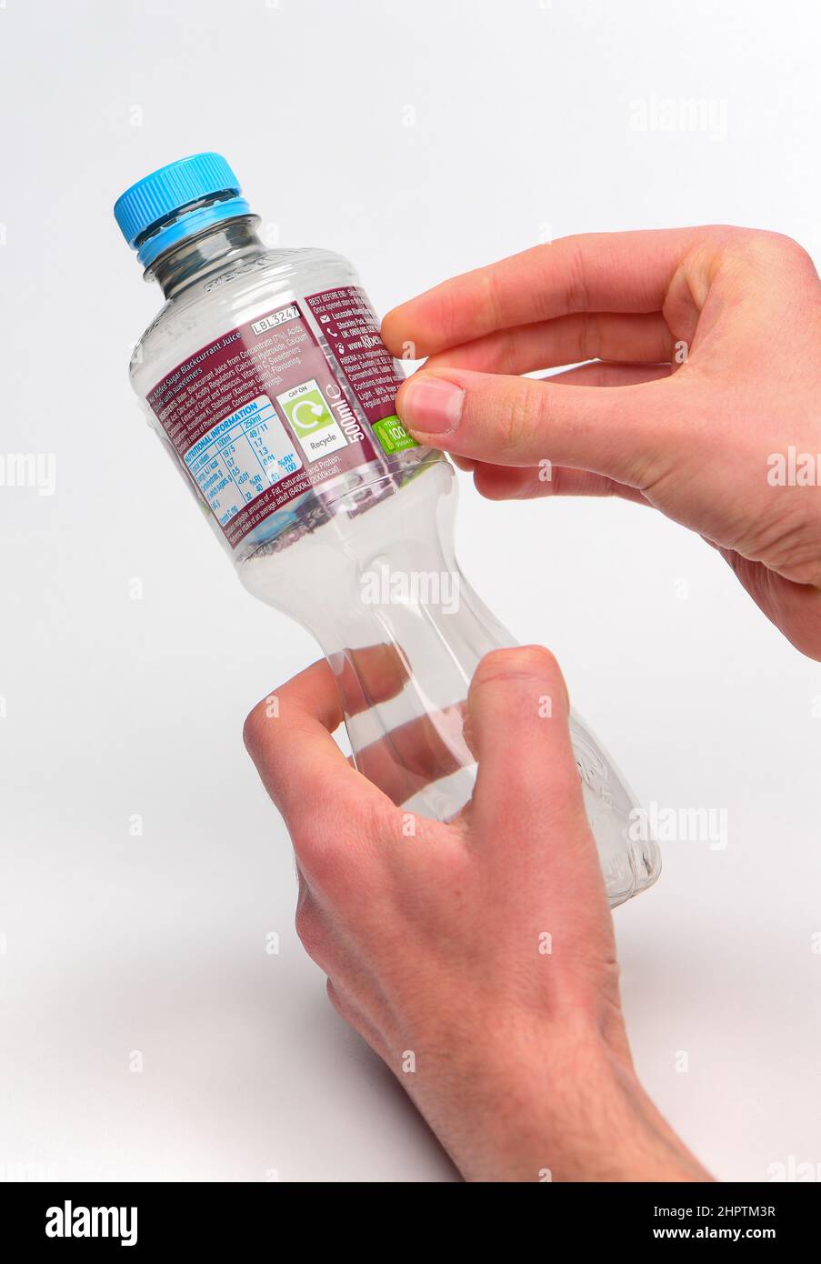 Removing label for recycling on a single use plastic bottle, bottle has a Ribena label and is photographed against a white background. Stock Photo