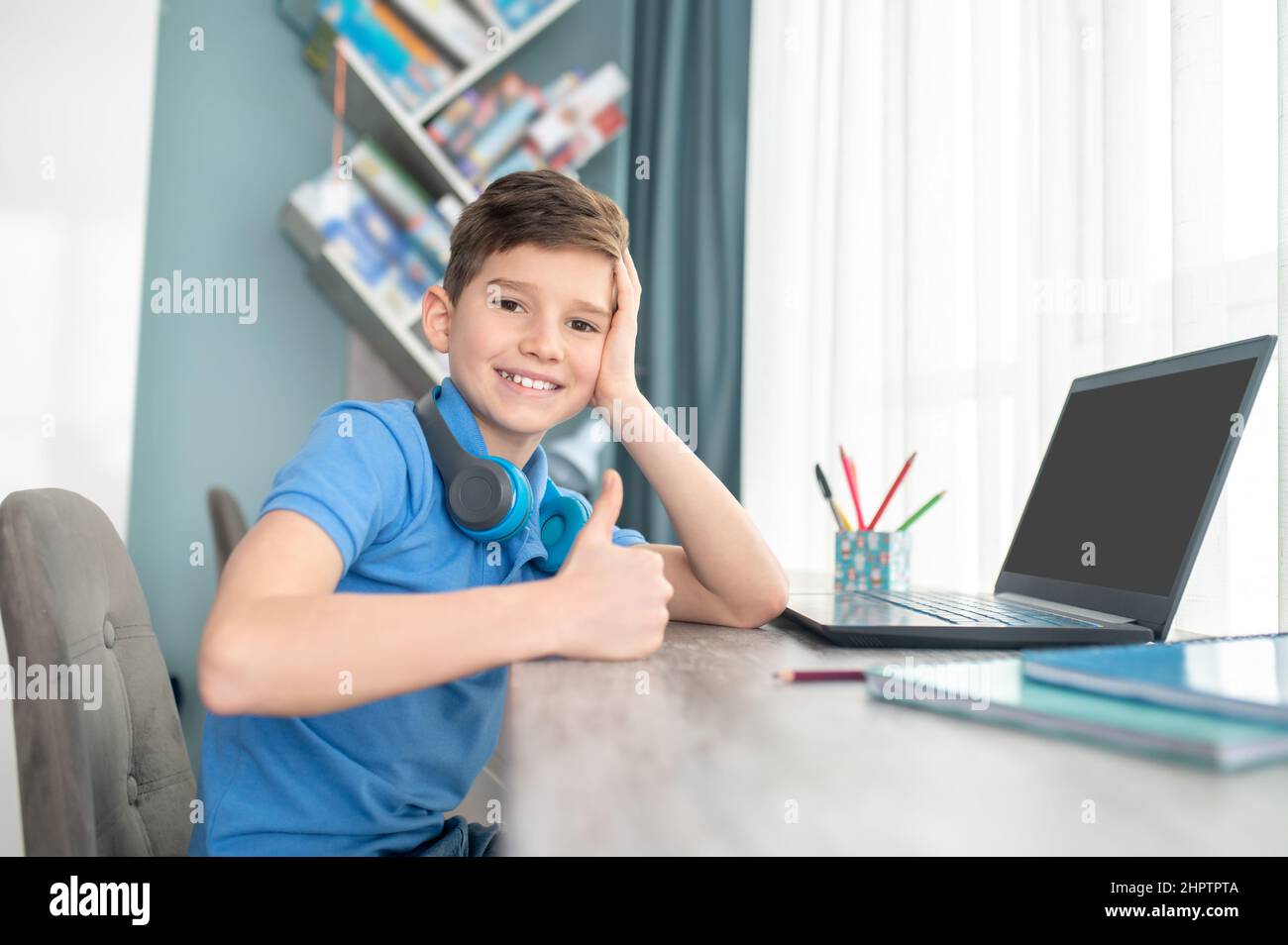 Joyous kid sitting in his room leaned on his desktop Stock Photo