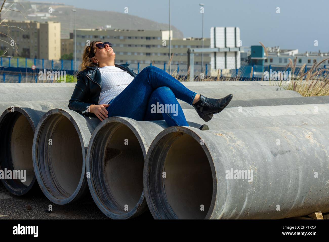 Caucasian woman with sunglasses lying and posing on reinforced concrete pipes in the industrial area Stock Photo
