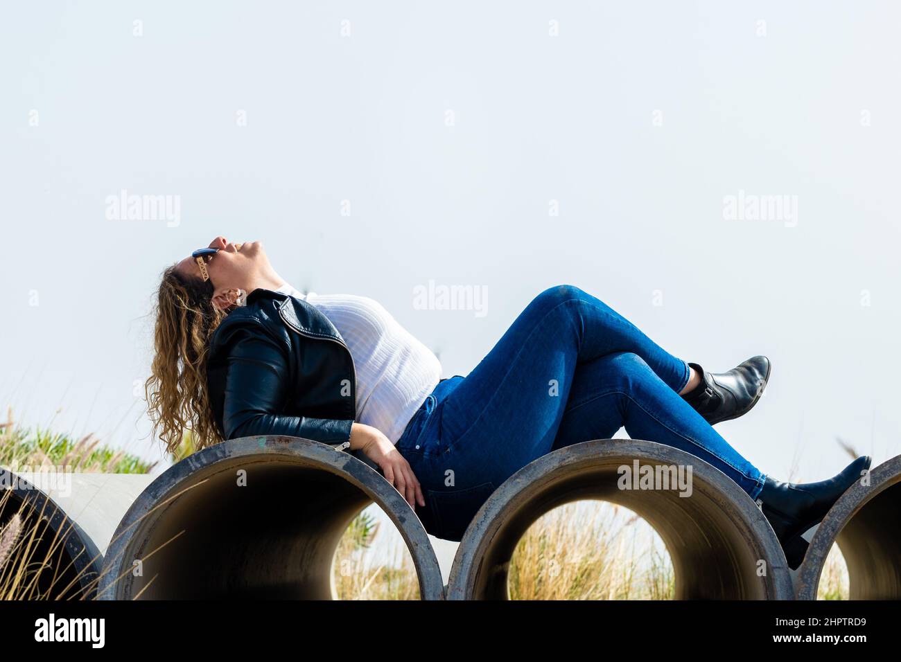 Caucasian woman with sunglasses lying and posing on reinforced concrete pipes in the industrial area Stock Photo