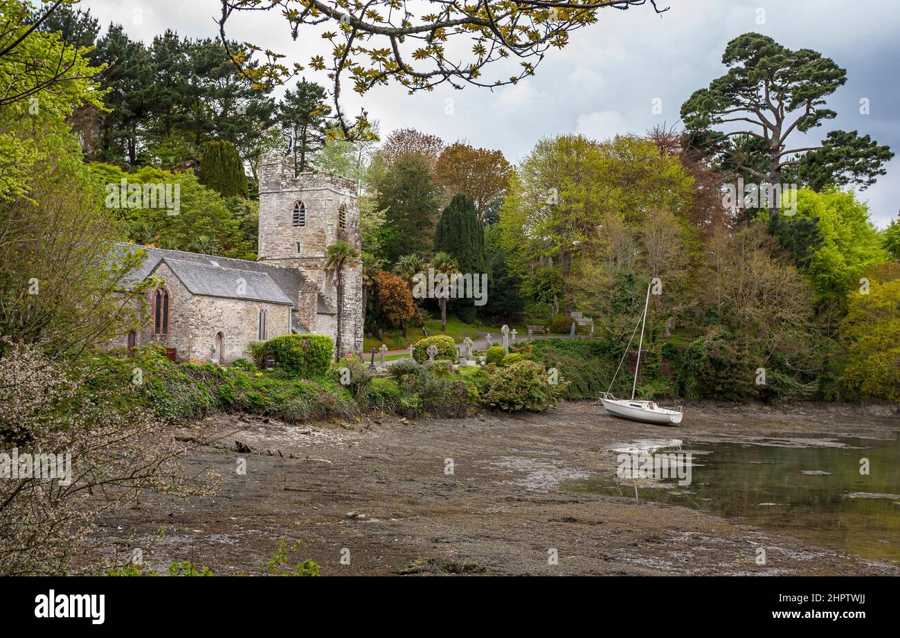 Sailing in to St. Just in Roesland: A small parish church on the south coast surrounded by a small cemetery and gardens.  A sailboat is drawn up on the beach. Stock Photo