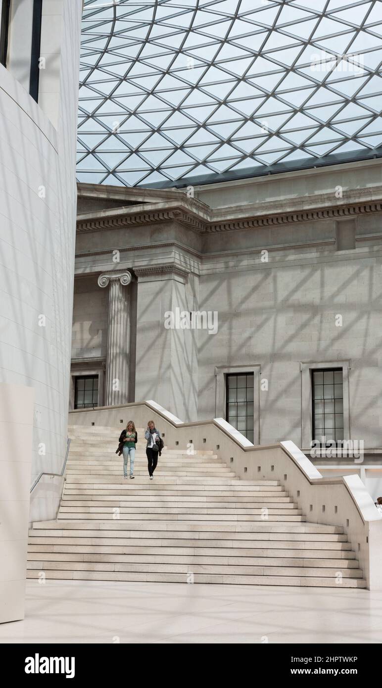 Grand Staircase under the dome of the Great Court: The Great Court at the British Museum now a bright indoor space thanks to a massive partial dome that encloses the space. Two woment walk down the stpes from the first level. Stock Photo