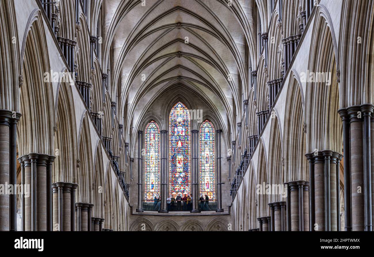 Columns and Rear Stained Glass at Salisbury: The ceiling and rear window of Salisbury Cathedral.  A tour goup pauses at the bottom of the window. Stock Photo