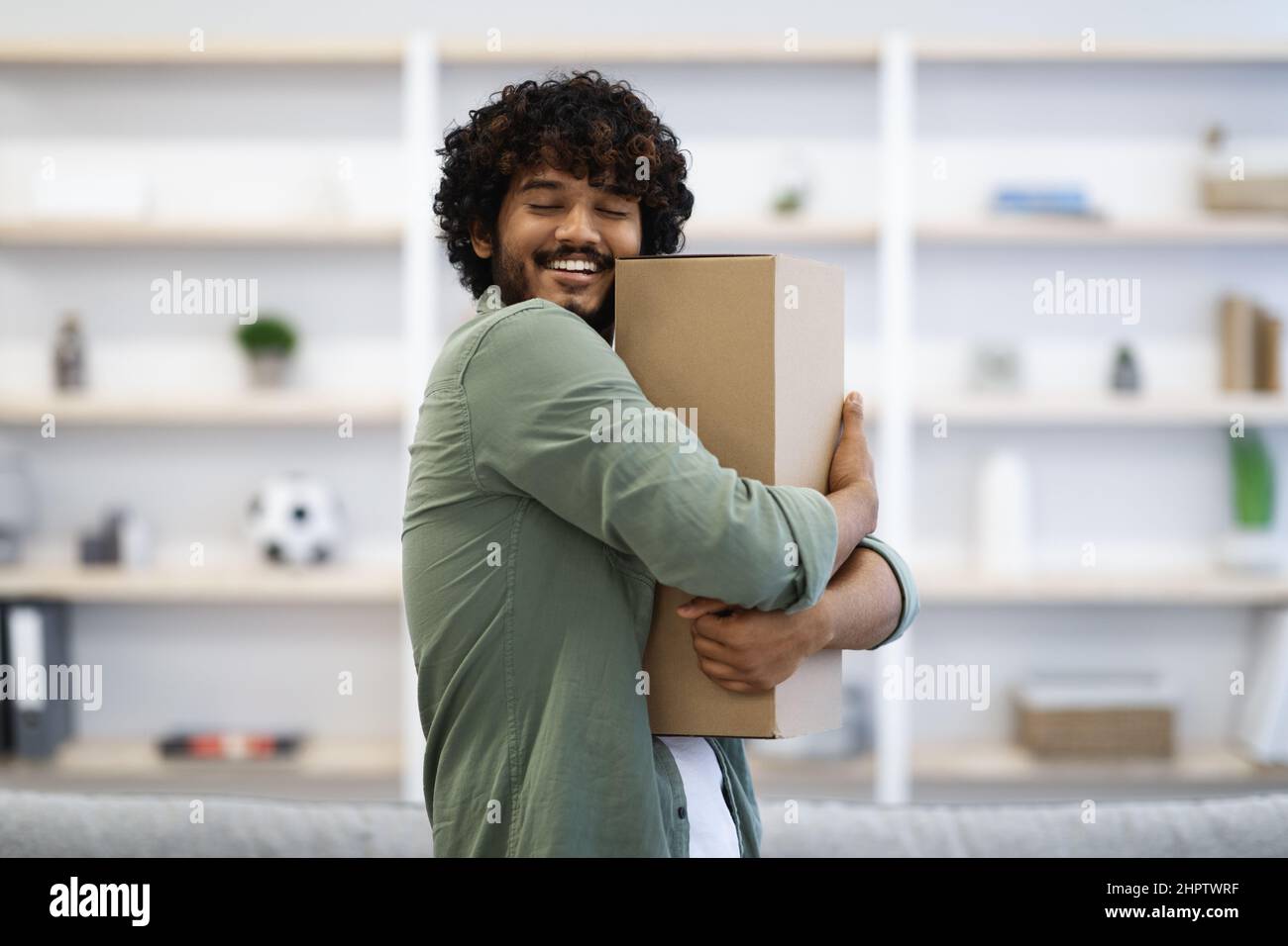 Ecstatic young indian man hugging box at home Stock Photo