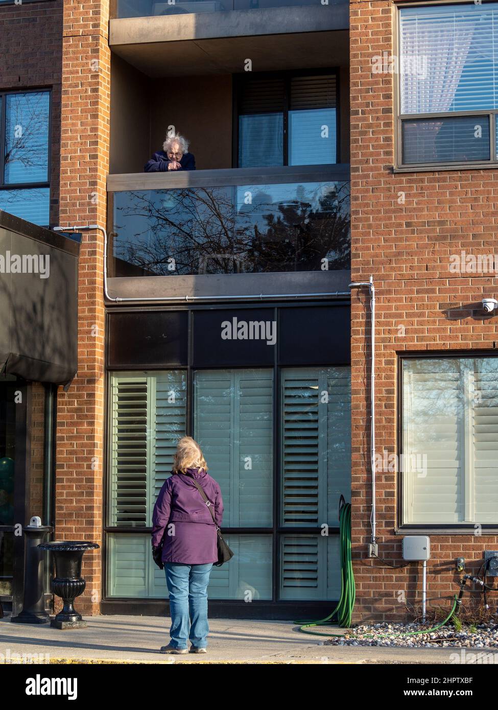 Distance visit during a pandemic lockdown: A woman visits with her mother perched above her on a second floor balcony during the COVID-19 pandemic of 2020 and 2021. Stock Photo