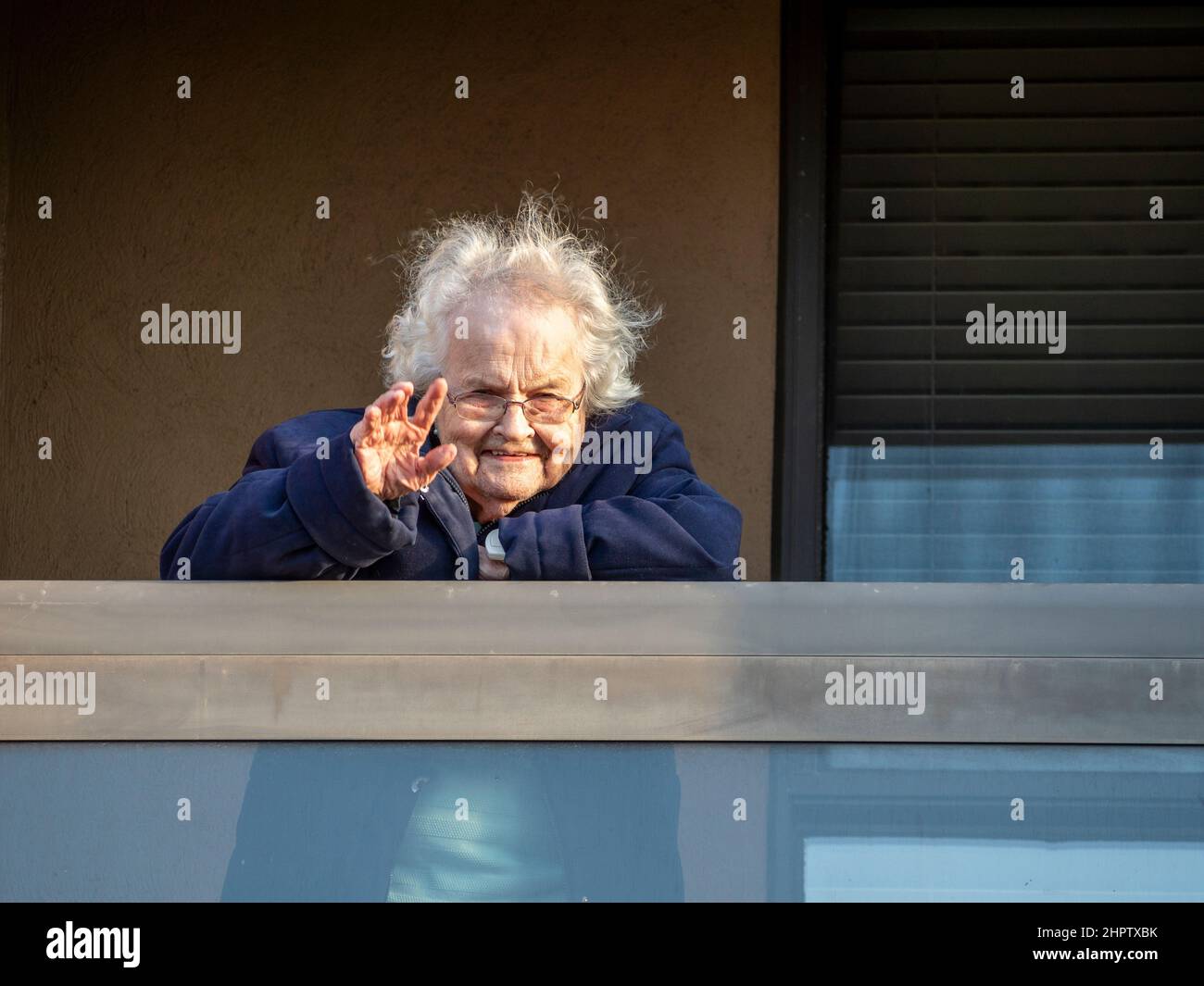 Wave visit to a Retirement home in Pandemic Lockdown: A senior woman waves from her balcony in an Ottawa retirement home during the 2020-2021 global COVID-19 pandemic. Stock Photo