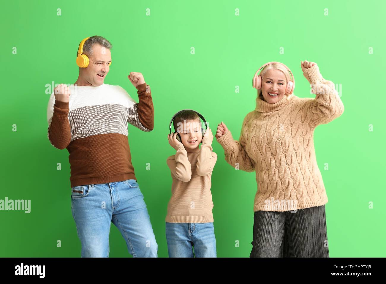 Little boy with his grandparents in headphones dancing on green background Stock Photo