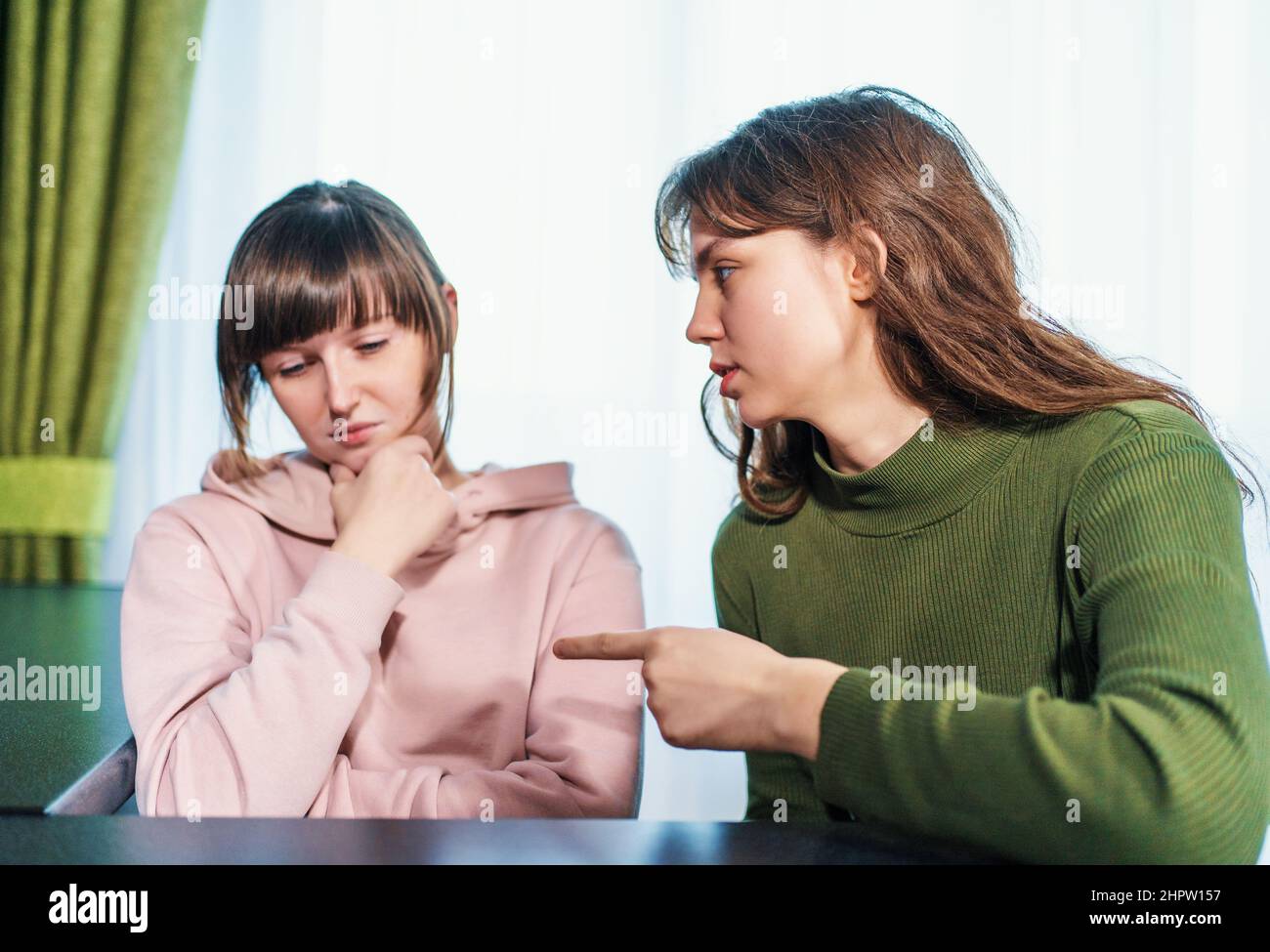 Young angry girl scolding or arguing her sad upset girlfriend, waving hand and poking her finger. Abuse and conflict relationship concept. Stock Photo