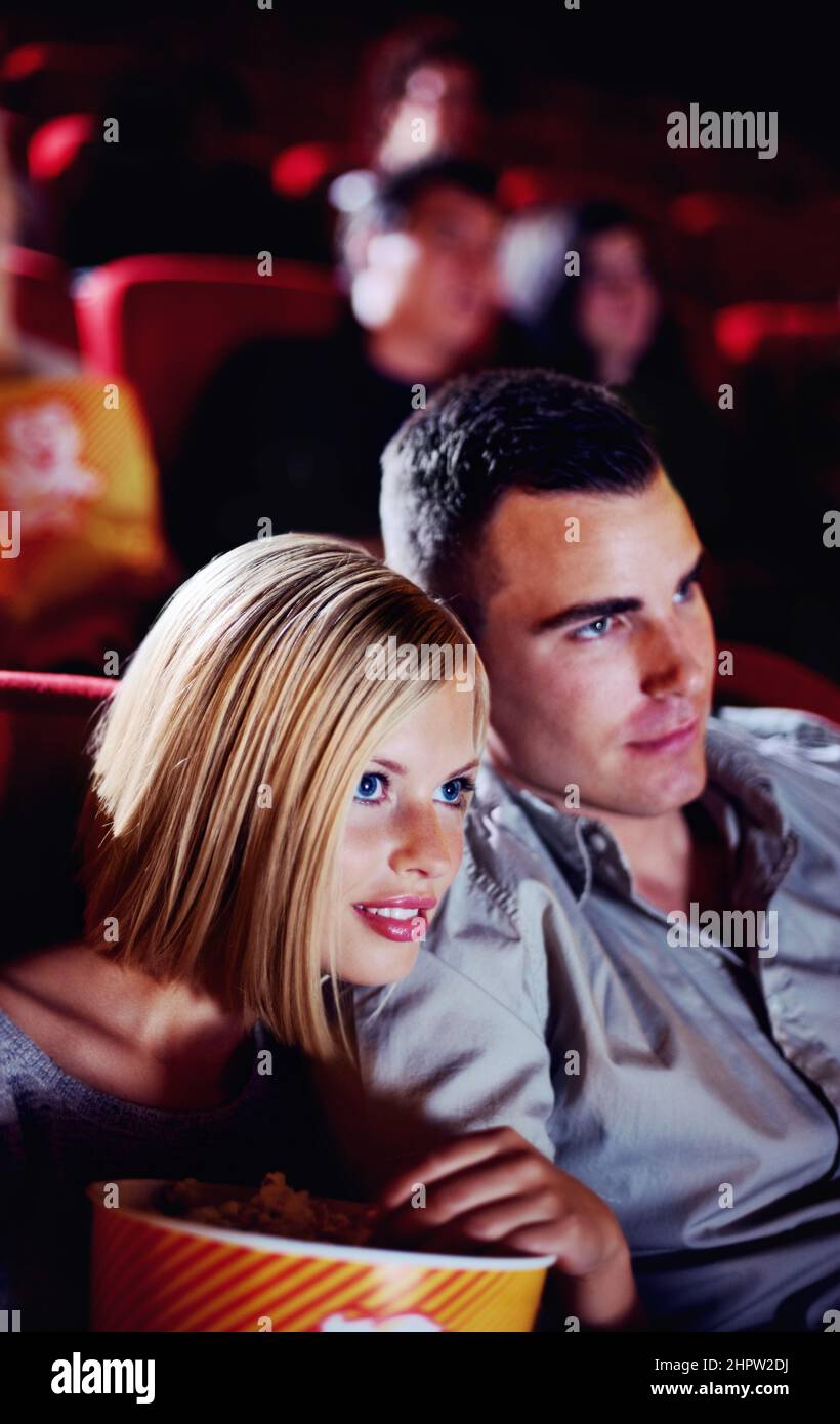 Here comes the scary part.... A cute young couple watching a scary movie in a cinema together. Stock Photo