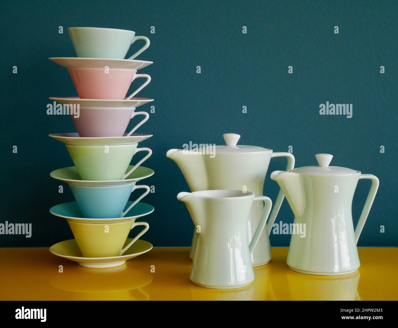 Stack of colorful vintage tea cups and tea pots on yellow table against