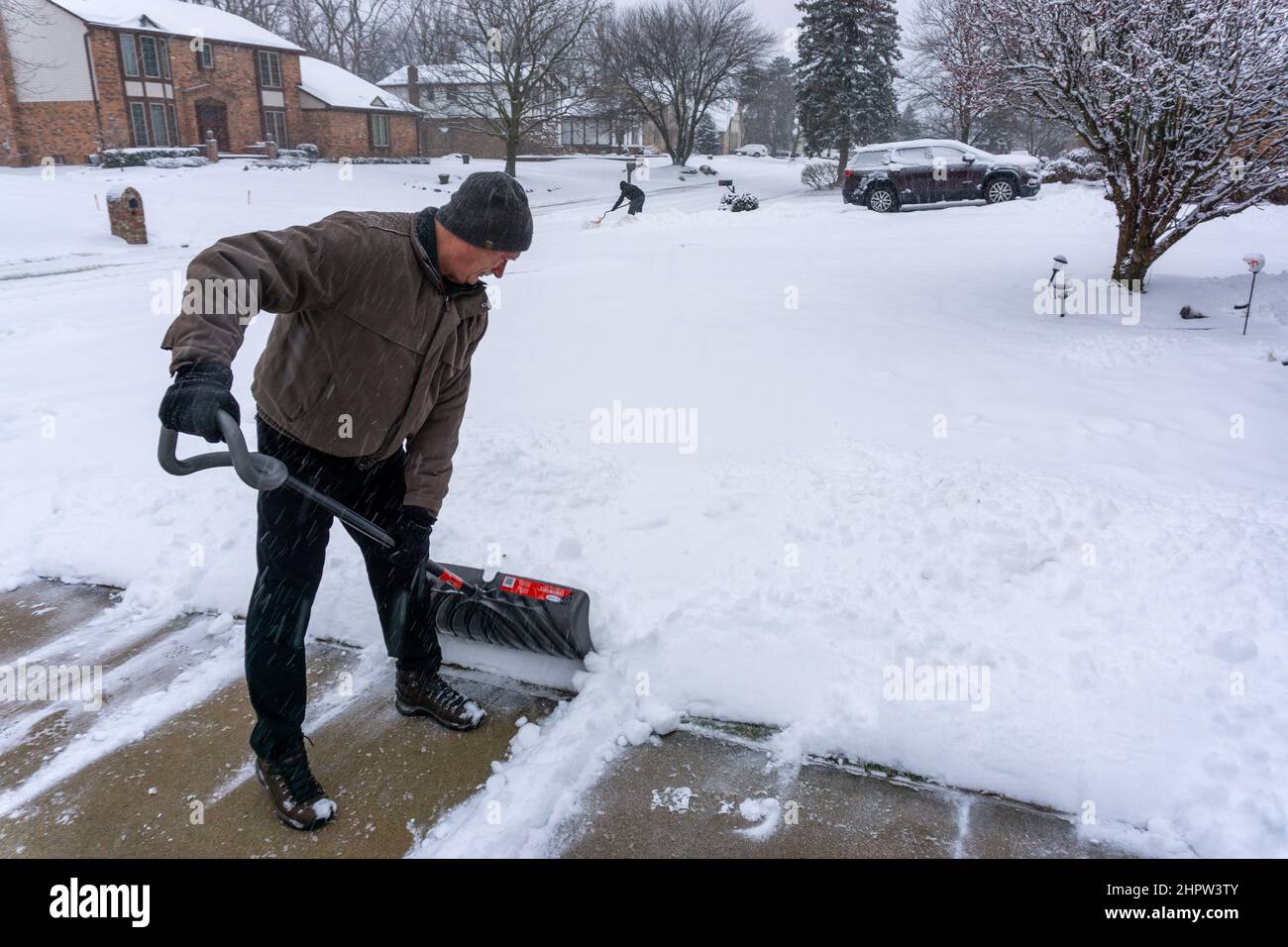Old retired man clears snow off of driveway Stock Photo