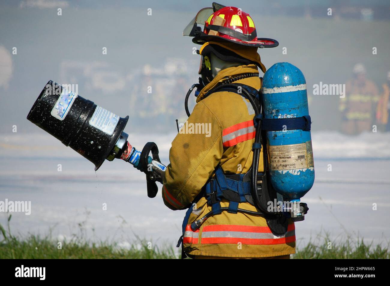 Firefighter in full turnout gear and self-contained breathing apparatus stands ready with foam nozzle Stock Photo