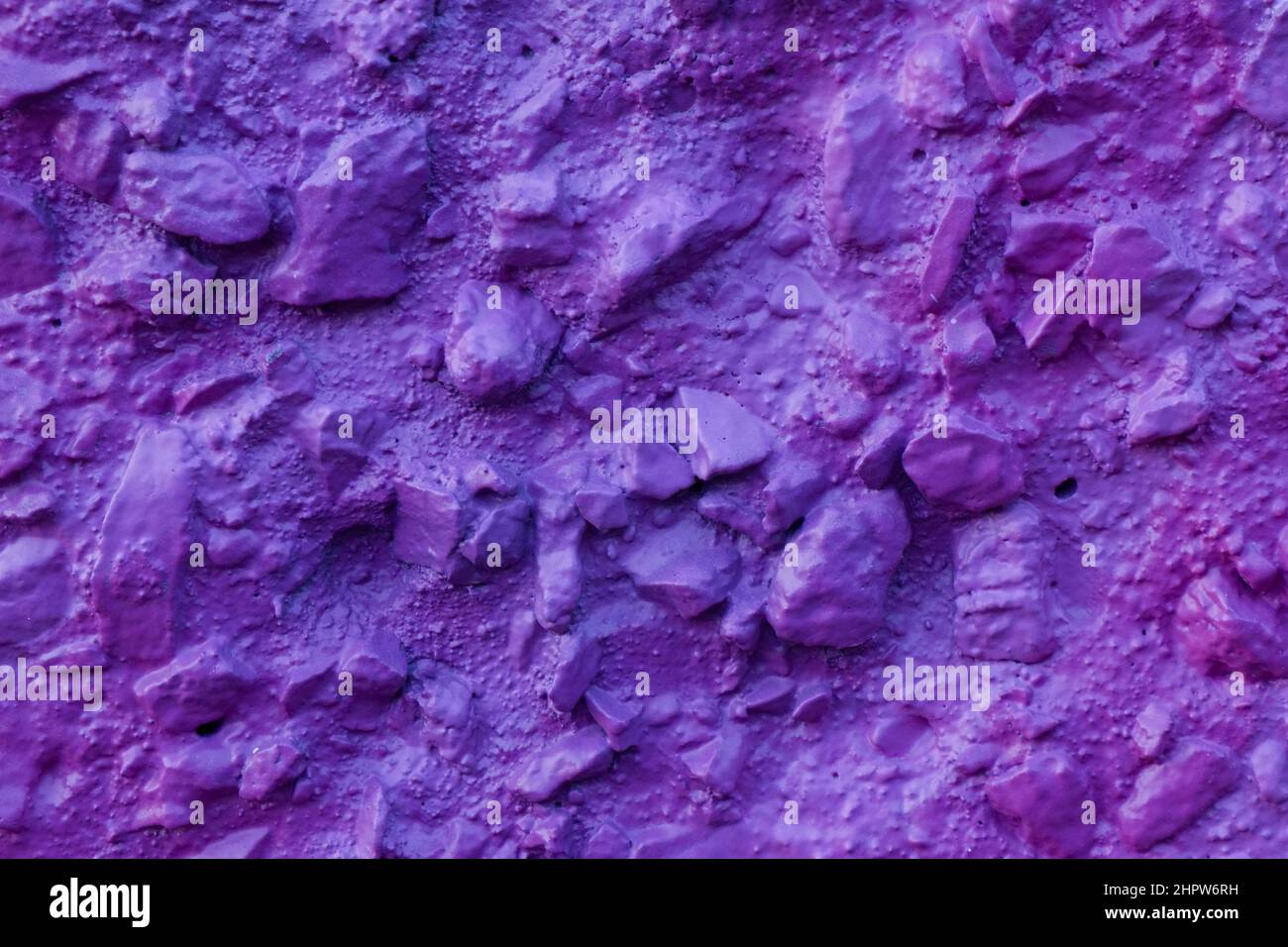 Violet painted relief wall with rough chaotic convex elements. Concrete wall covered uneven decorative stucco and painted bluish-purple paint. Stock Photo