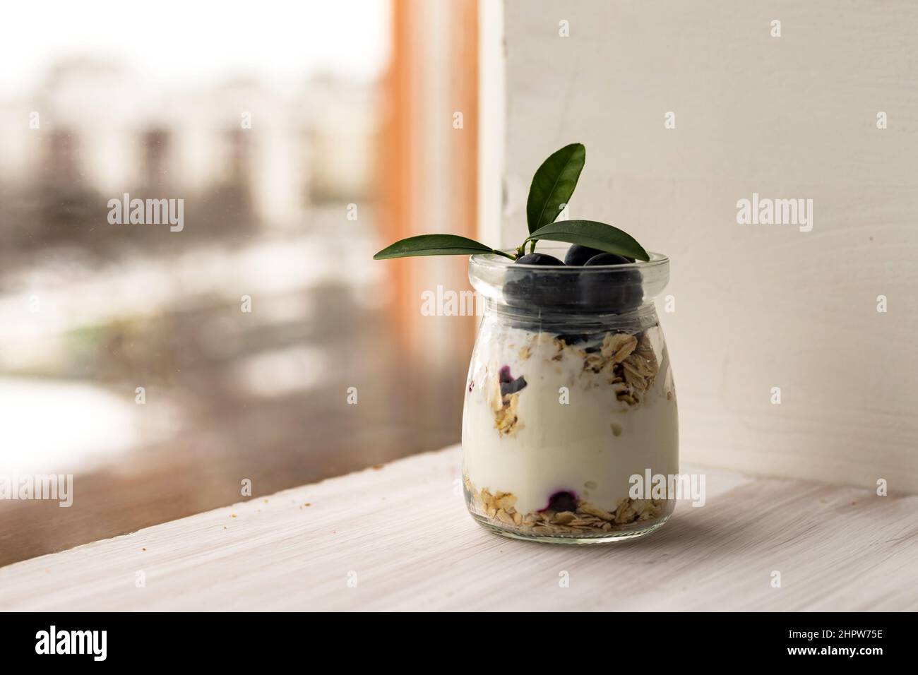 Oatmeal muesli granola with yogurt, blueberry parfait, overnight oats in glass jar on white table Stock Photo