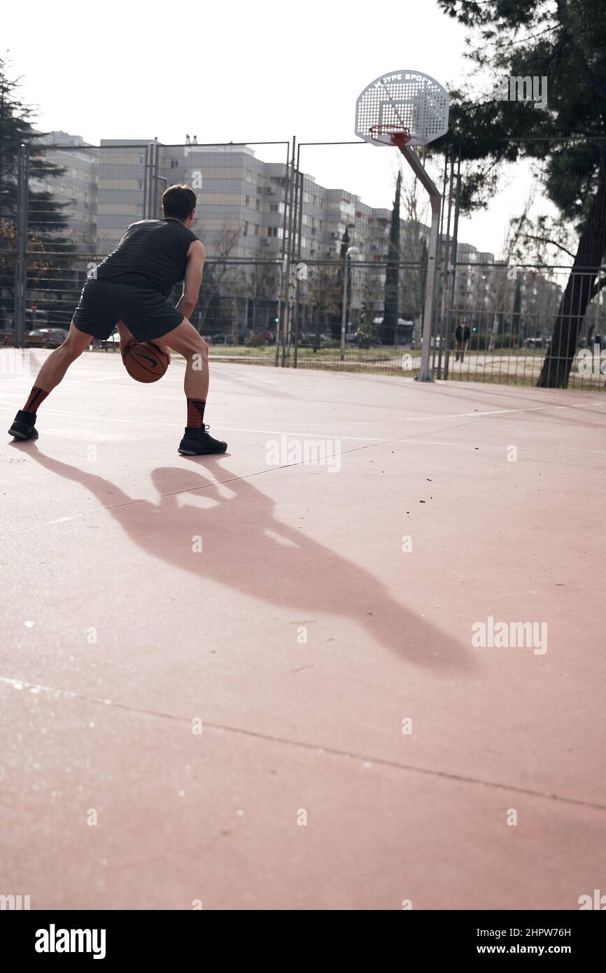 young man playing basketball outdoor on street with long shadows Stock Photo
