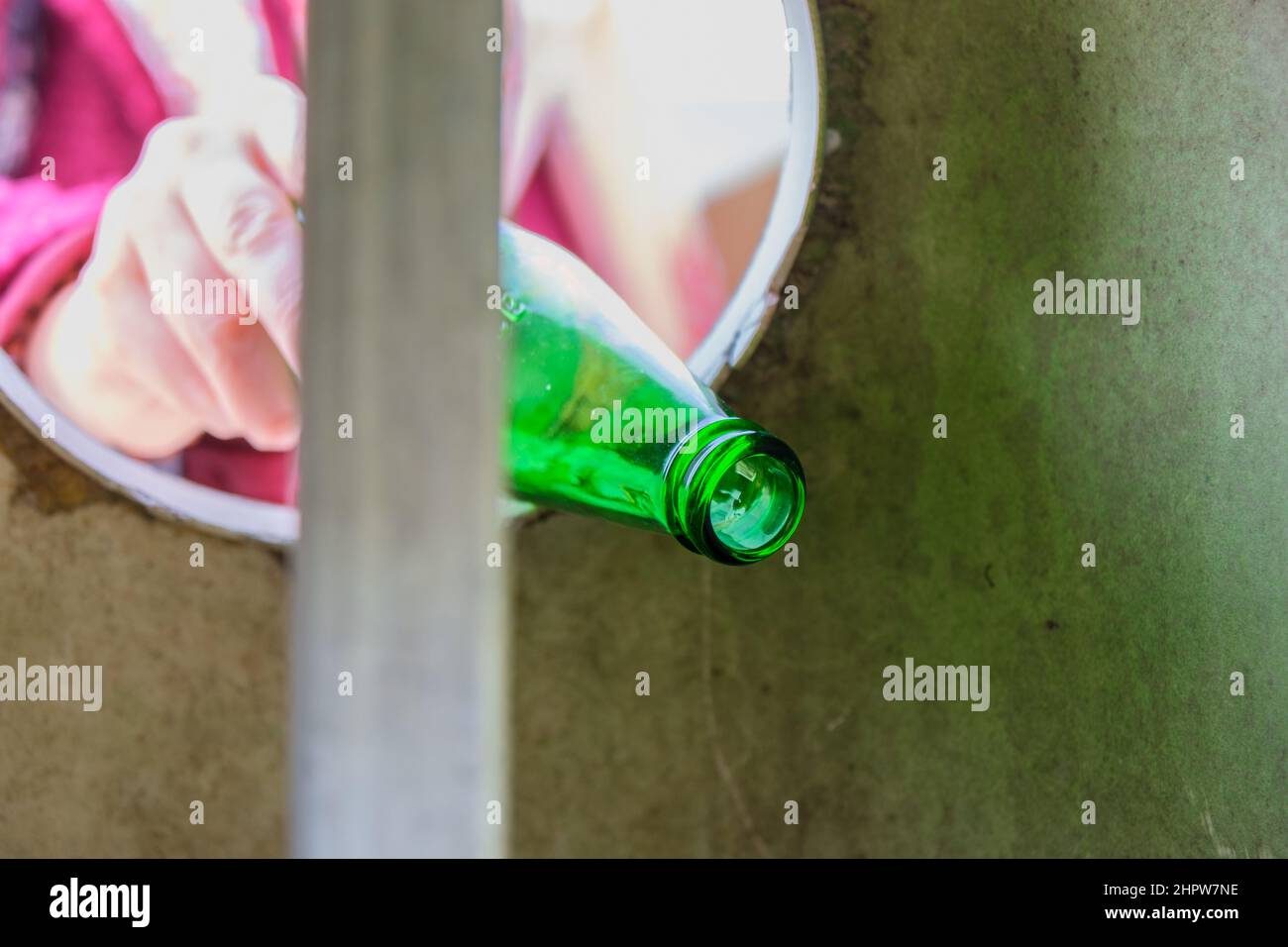 Woman or female hand throwing empty green glass bottle into recycle bin garbage container. Nature love, waste sorting, recycling, caring concept idea. Stock Photo