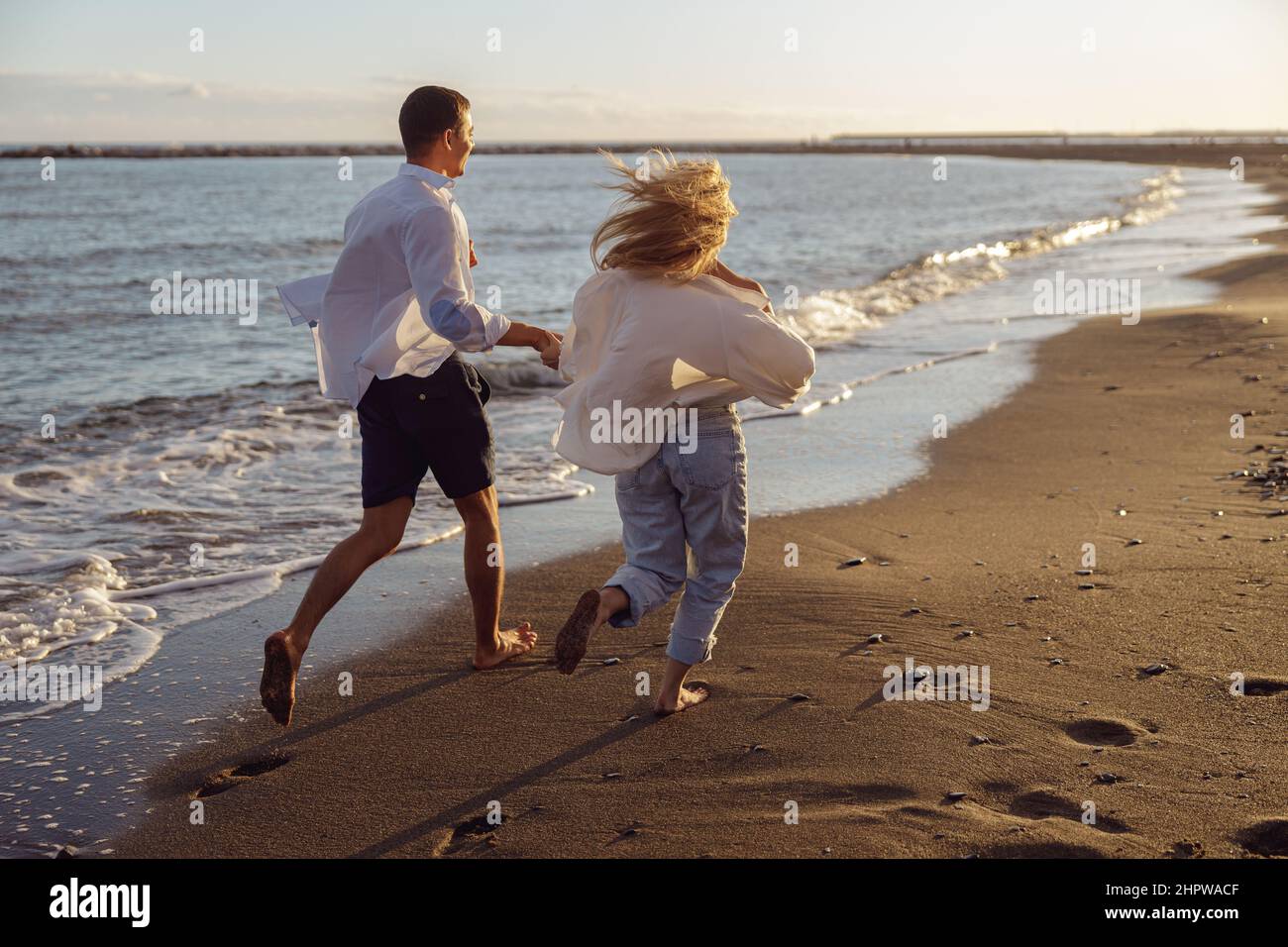 Back photo of man and woman running holding hands along the ocean Stock Photo
