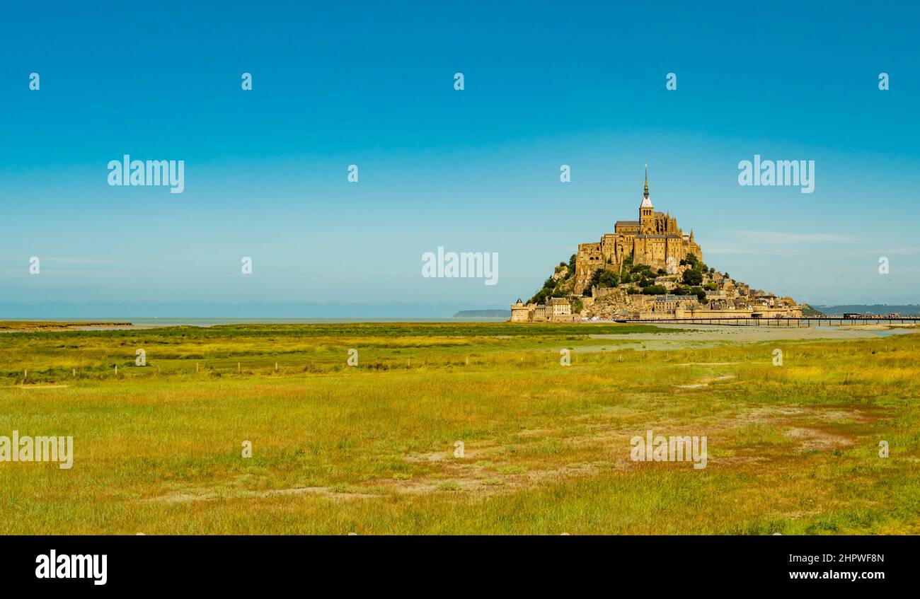 Stunning view of famous Le Mont Saint Michel tidal island on a bright sunny day with empty green fields, Normandy, Northern France Stock Photo