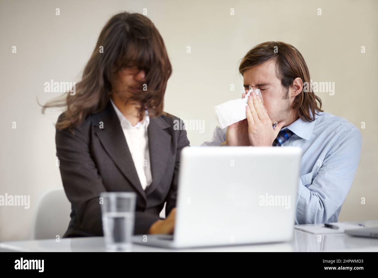 Showing poor manners. A young businessman blowing his nose all over a coworker. Stock Photo