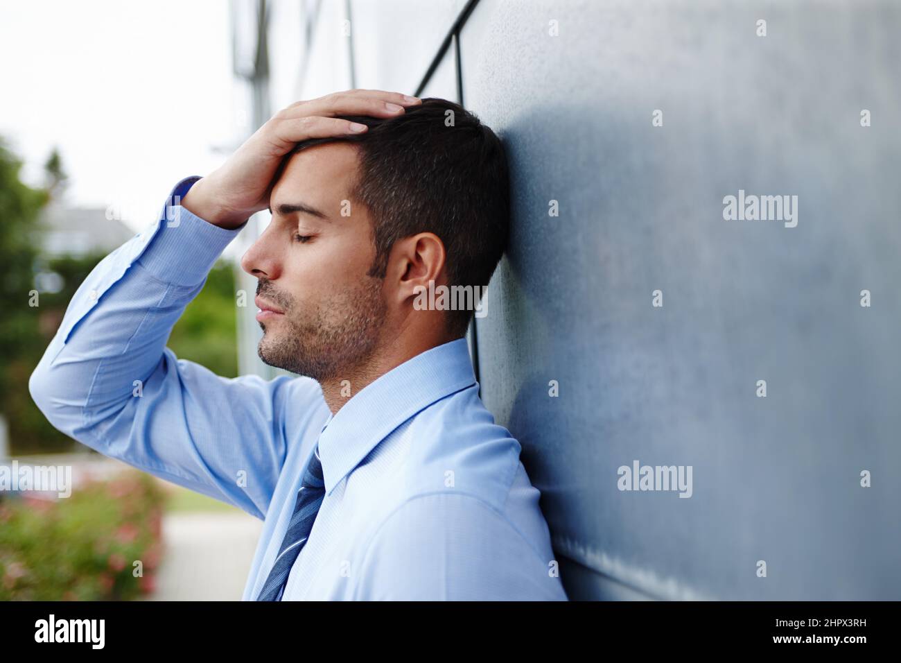 Fired.... A stressed young businessman standing outdoors with his head in his hands. Stock Photo