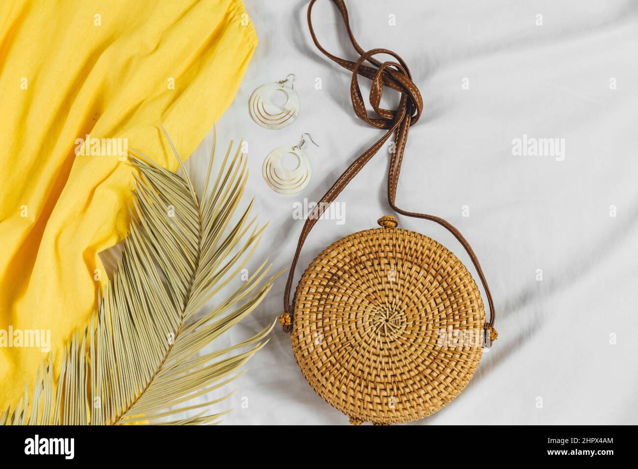Straw hat, yellow dress, straw bag on white background. Trendy summer outfit. Flat lay with clothes for holidays and vacations. Stock Photo