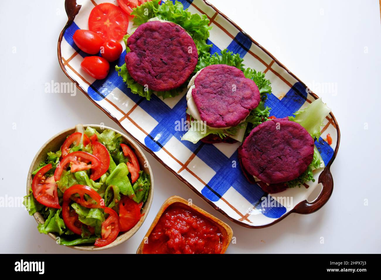 Amazing colorful raw material food for vegan hamburger from violet sweet potato with tomato sauce, salad, cucumber, healthy food for breakfast that ri Stock Photo