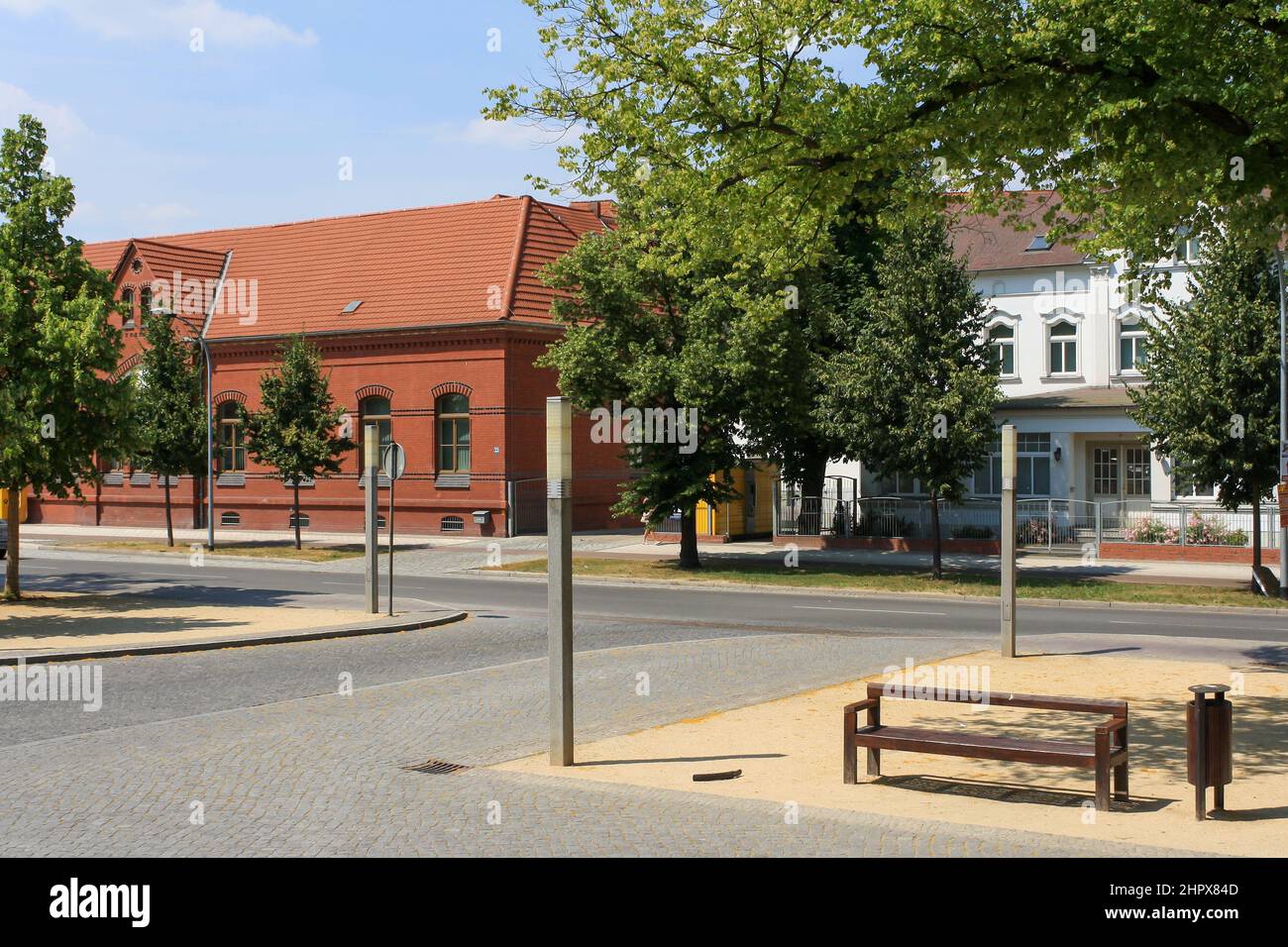 View of bench in park at Stendal train station in Germany with summer clear blue sky. Old building exterior in background. No people. Stock Photo